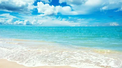 Clear aqua water laps a pale sand shelf under puffy clouds, sunlight glittering across the surface — the plain sand strip works well under desktop icons.