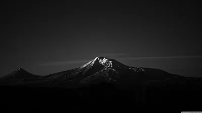 A single peak keeps the last light on its snowfields while the sky and foreground drop away to black.