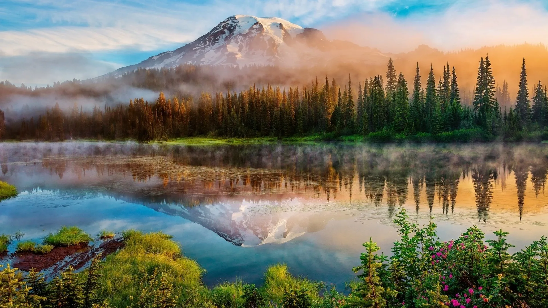 Morning fog slides across the water as sunrise colours the firs gold, the snowcap doubling in the still lake; the mirrored peak lands mid-frame, so a centre crop holds.