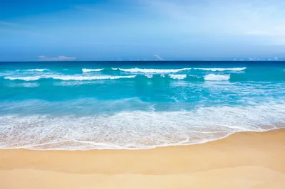 Ranks of small waves stack to the horizon under a pale sky, the wide golden sand strip below staying empty for icons or a dock.
