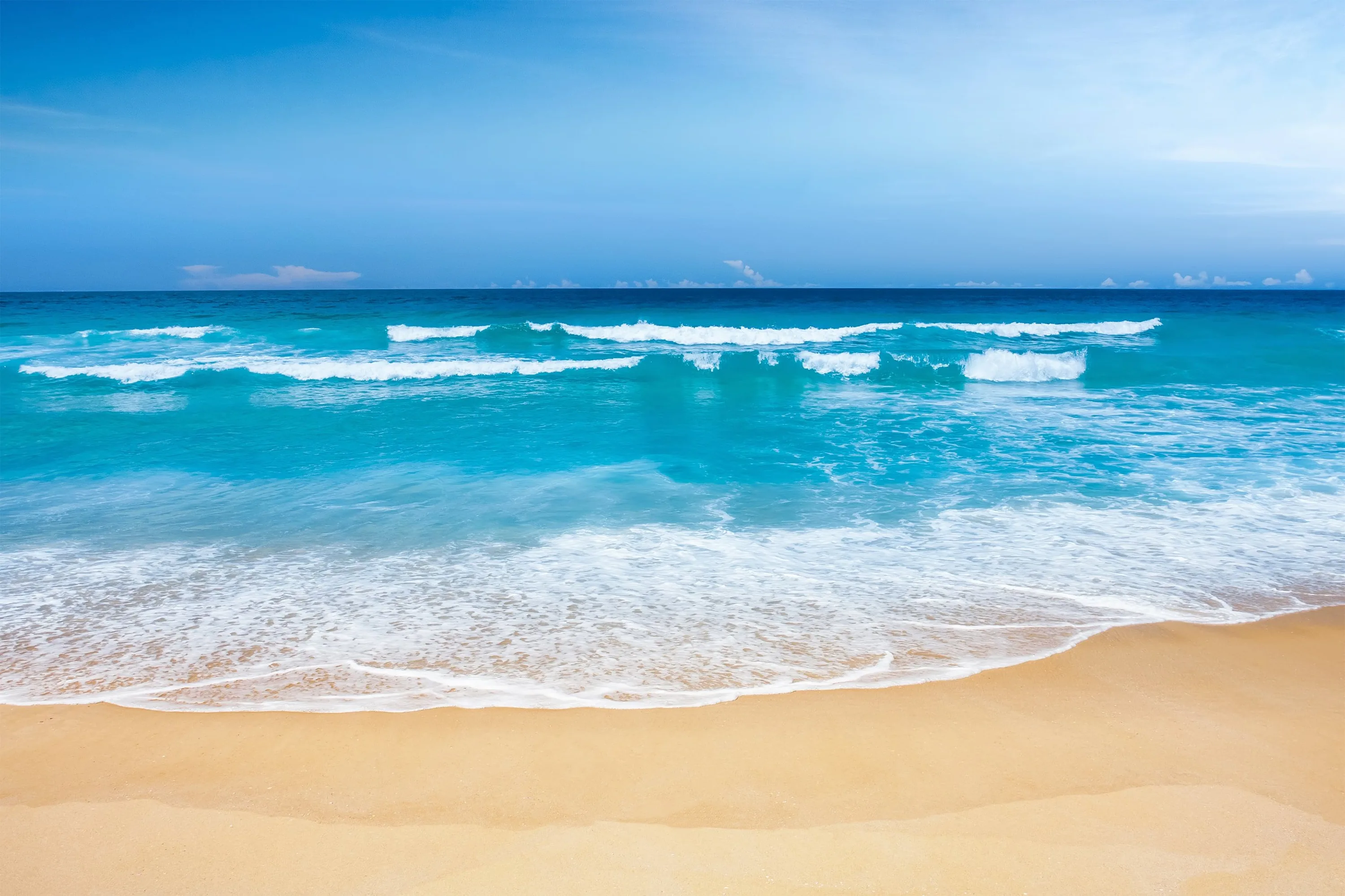 Ranks of small waves stack to the horizon under a pale sky, the wide golden sand strip below staying empty for icons or a dock.