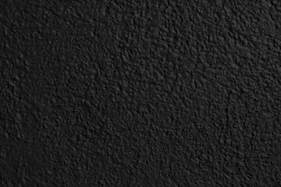 Thick textured paint over rendered wall, shot close so the grain reads as thousands of tiny raised bumps under a flat matte black.