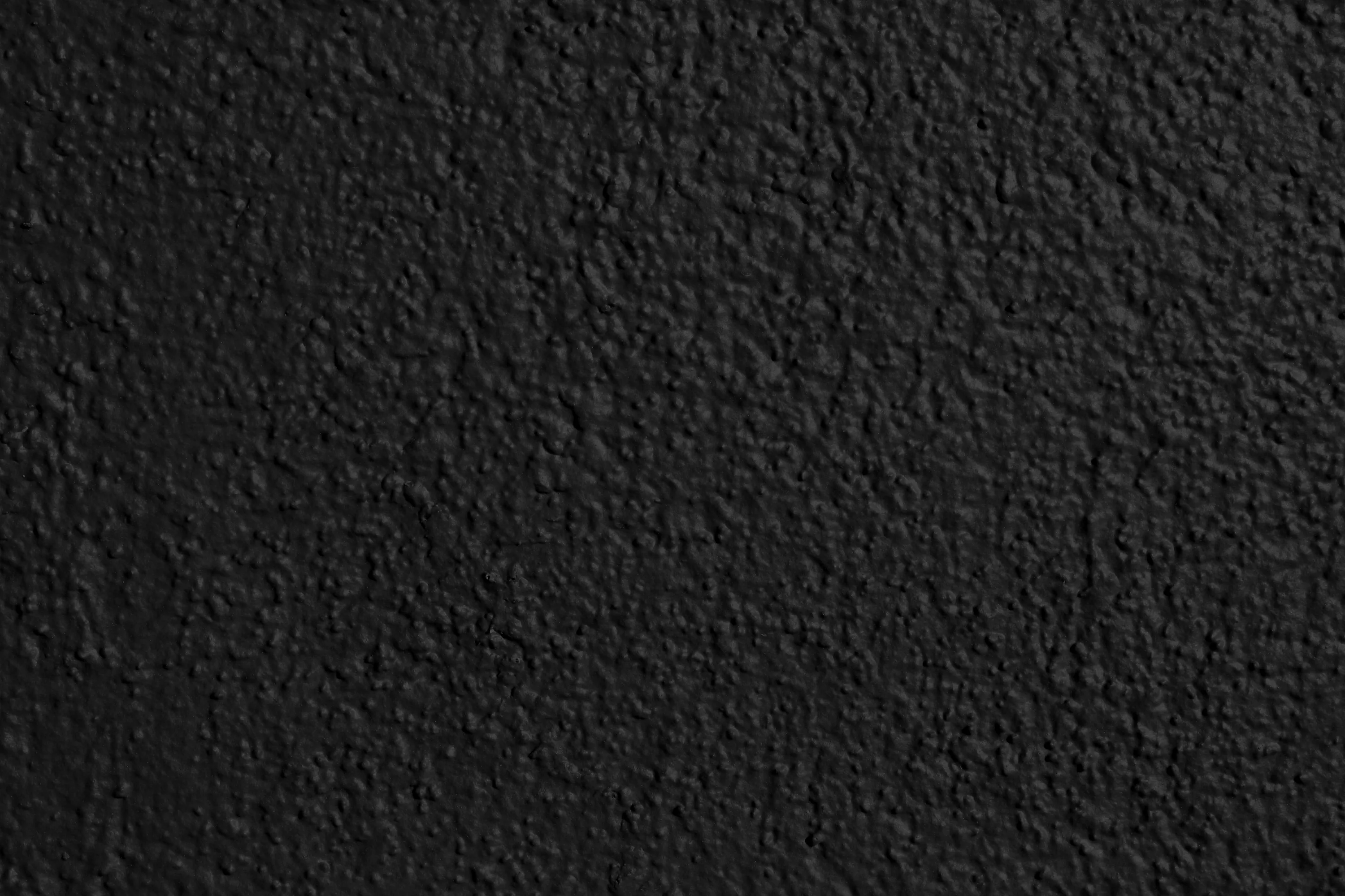 Thick textured paint over rendered wall, shot close so the grain reads as thousands of tiny raised bumps under a flat matte black.