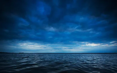 Heavy blue-grey clouds hang over a calm sea, a thin pale strip of sky at the horizon; the rippled foreground is dark enough for white text.