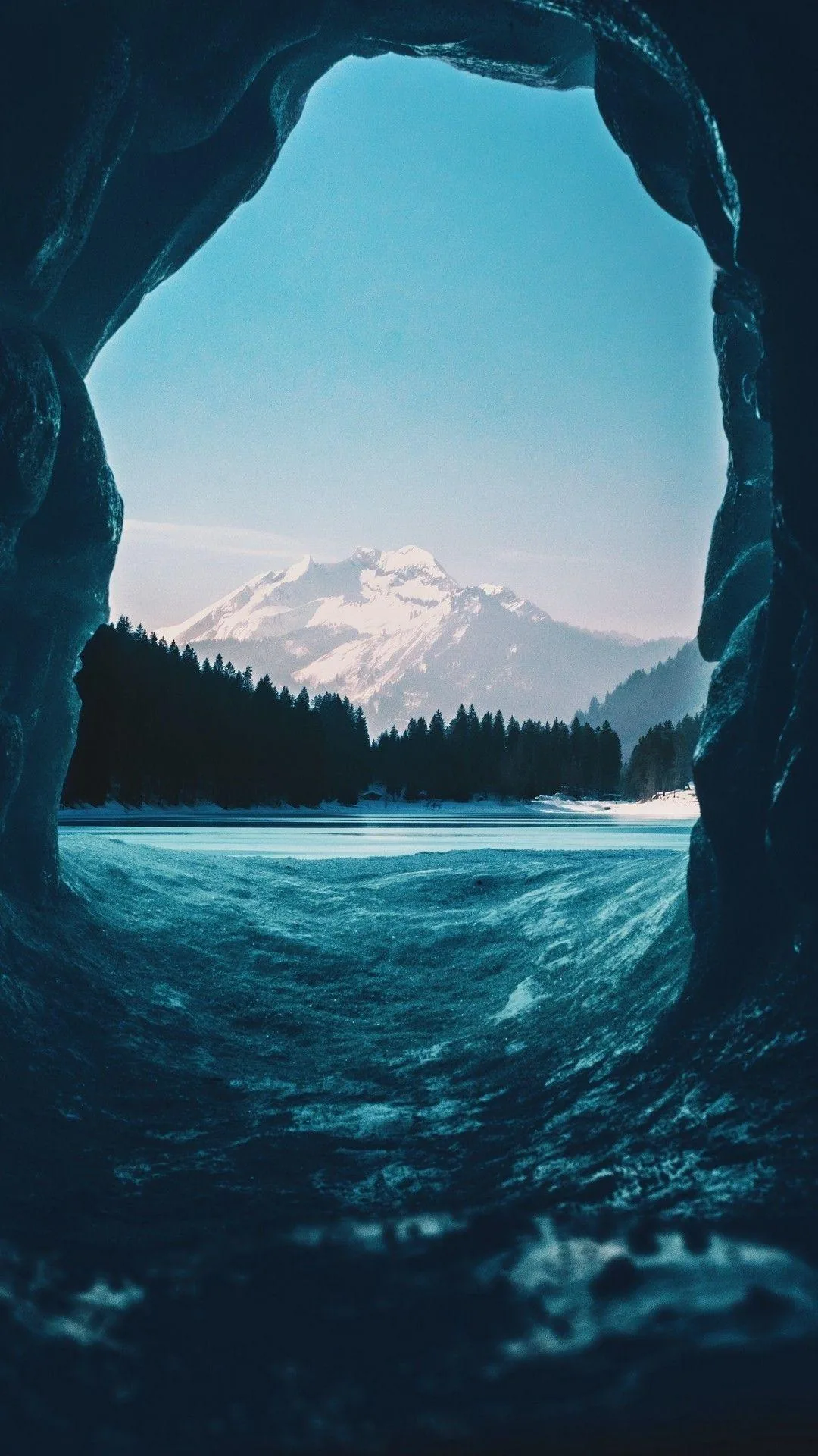 Shot from inside a glacier cave, blue ice arches around a distant snow mountain; the dark cave walls keep status icons readable along both edges.