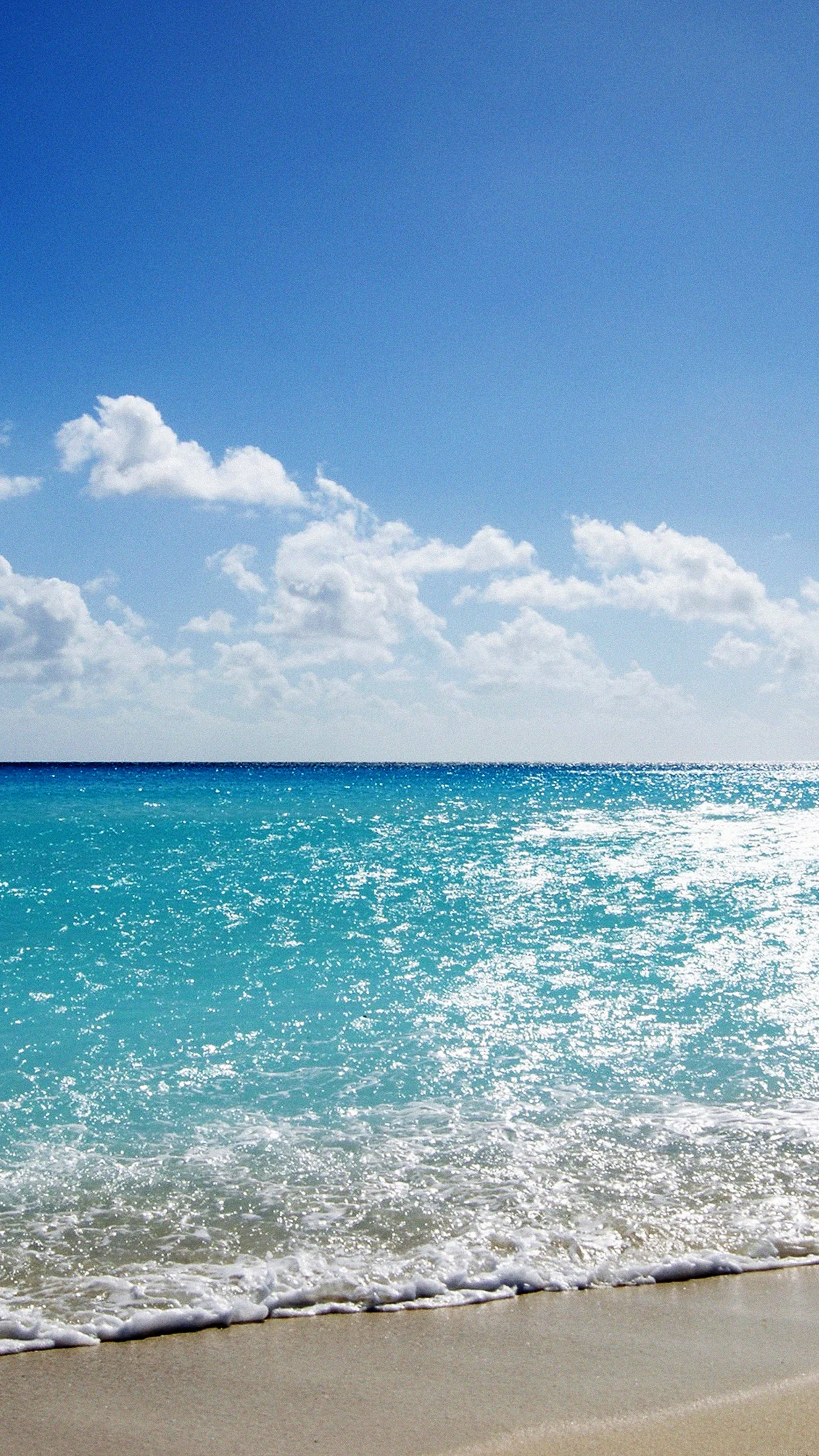 Open water glitters from the horizon down to a sliver of sand, and the tall empty sky above leaves the whole top half for the clock.