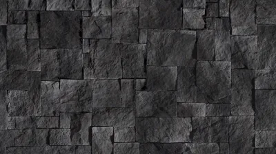 Rough-cut charcoal stone blocks interlock in staggered courses, side light raking across so every chipped edge throws its own shadow.