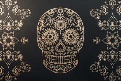 A Day of the Dead skull drawn in fine gold line work sits between two symmetrical floral flourishes on a matte black ground.