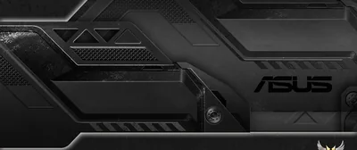 An ultrawide close-up of a laptop lid in brushed gunmetal, angular vents and the ASUS mark catching a low sidelight.