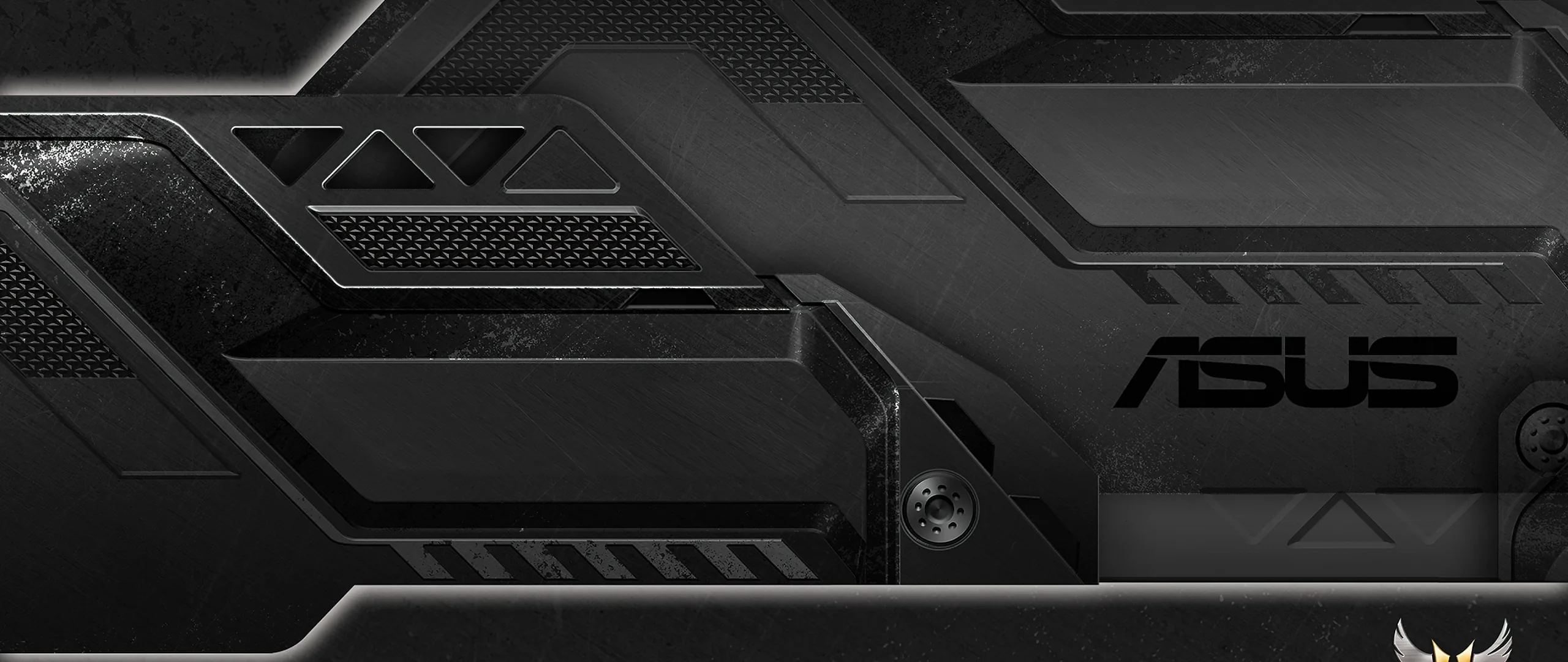 An ultrawide close-up of a laptop lid in brushed gunmetal, angular vents and the ASUS mark catching a low sidelight.
