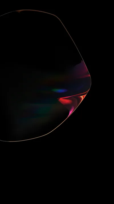 A soap-bubble form floats in the dark with only its rim visible, red and blue refraction gathering along one side against pure black.