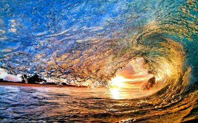 Seen from inside the tube, a curling wave wraps around a window of orange sunset light, the water's face patterned in gold and blue.