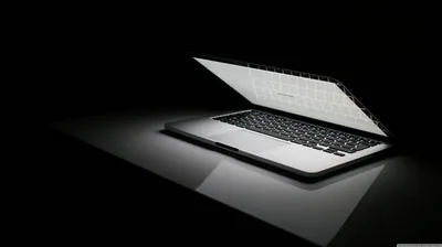 An open laptop throws light across a glossy black surface, its reflection stretching toward the bottom.