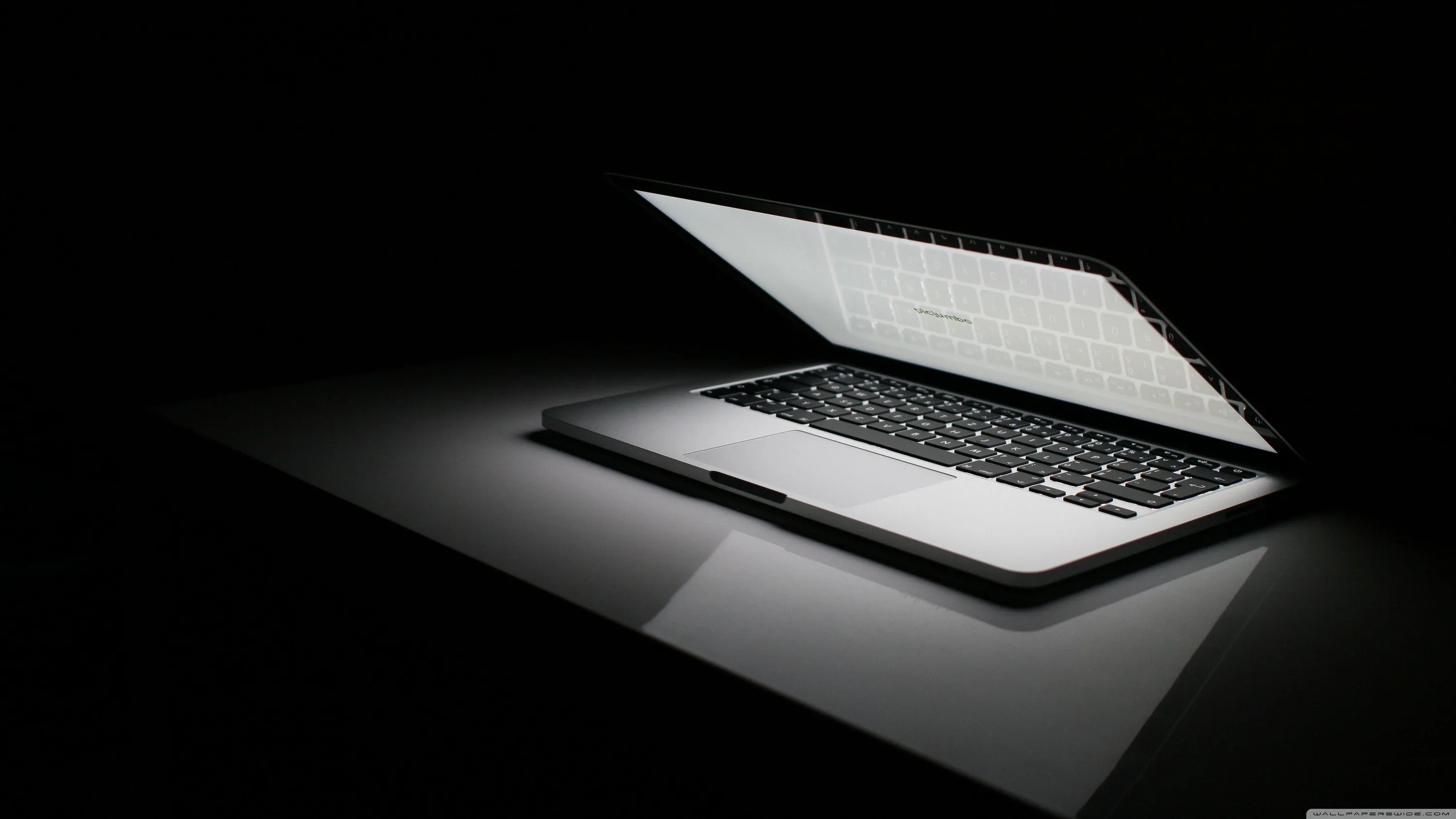 An open laptop throws light across a glossy black surface, its reflection stretching toward the bottom.