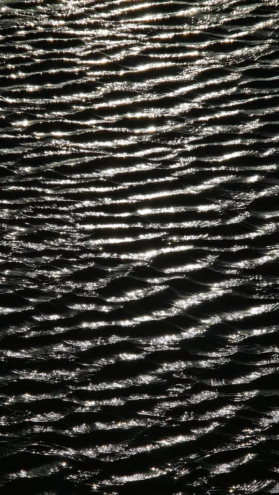 Close-up of water pushed into fine parallel ripples, each crest caught in silver against water that reads pure black.
