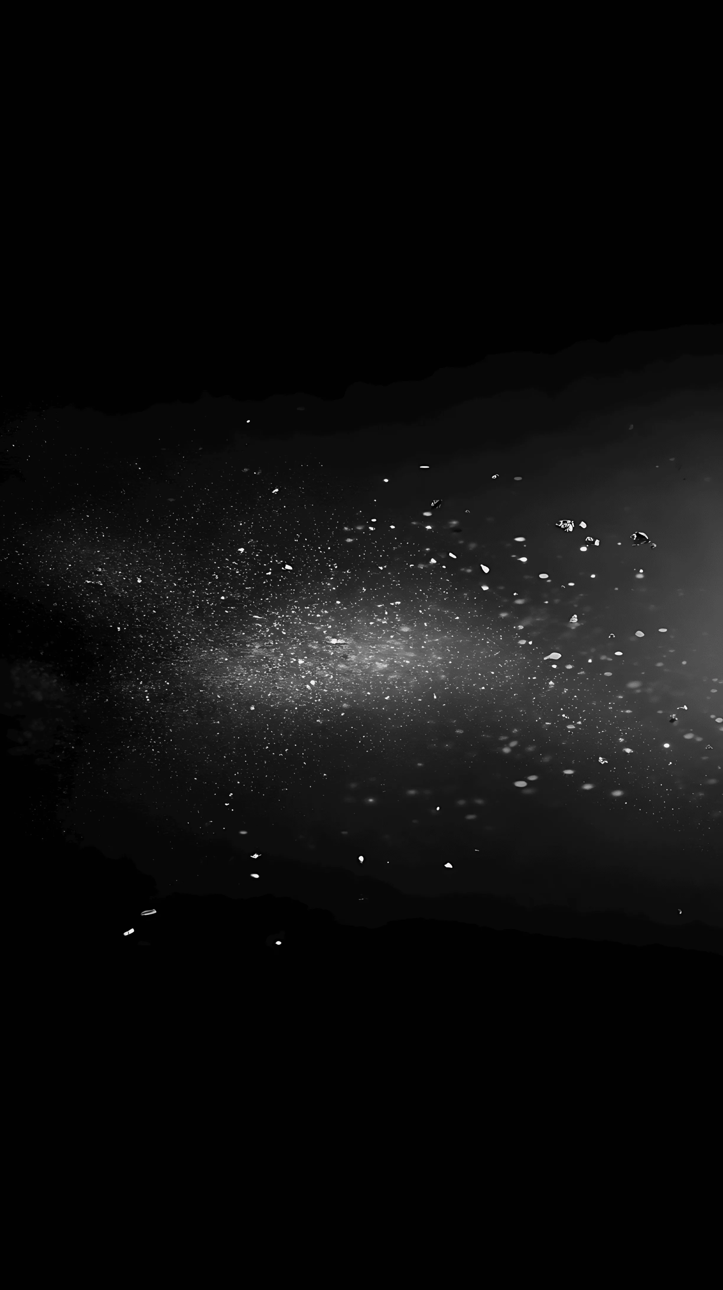 A pale wash of light and scattered specks spreads from one edge into deep black — a nebula seen dimly.