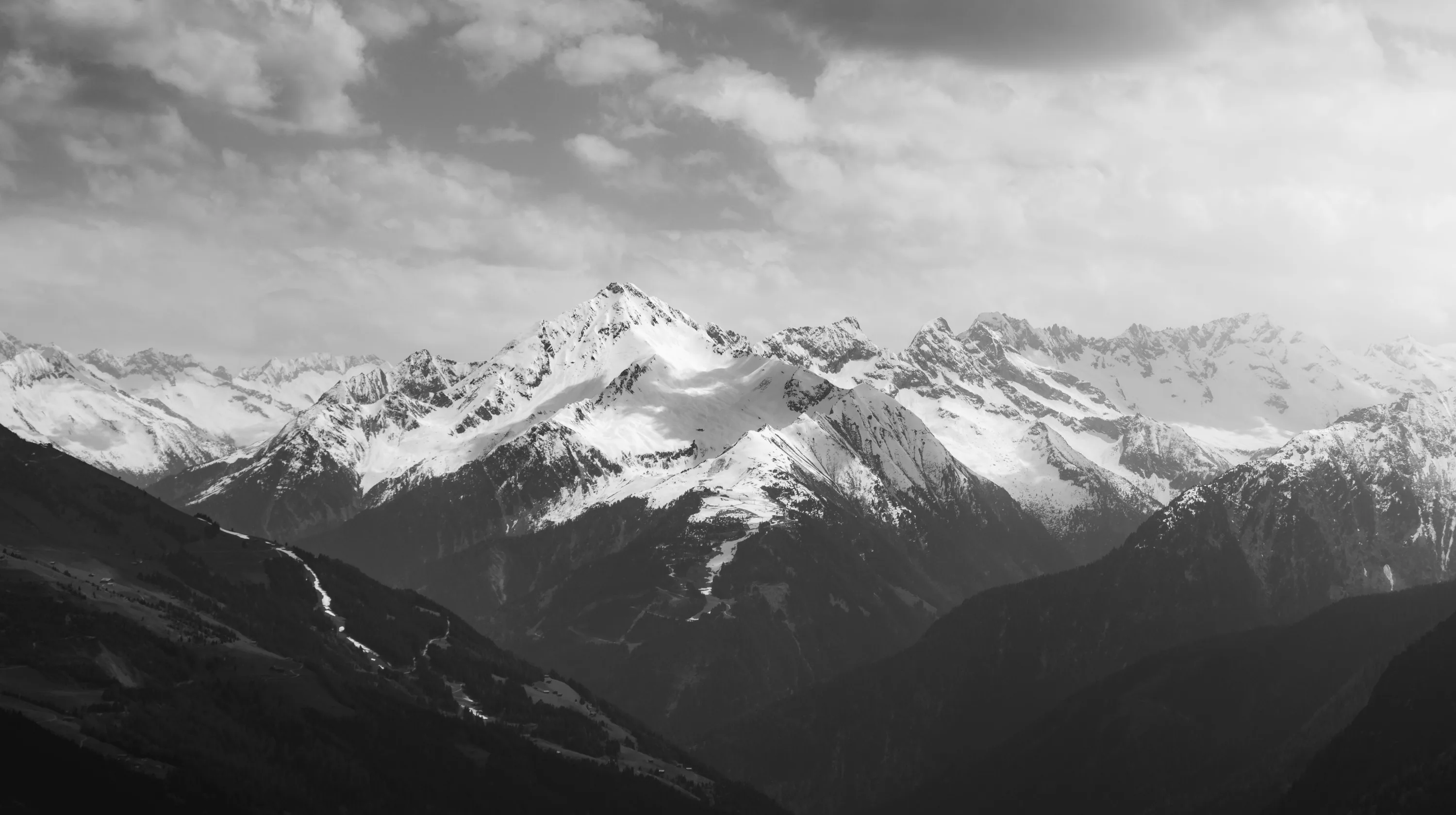 A range of snow-covered ridges runs across the middle distance in monochrome, the near slope in shadow.