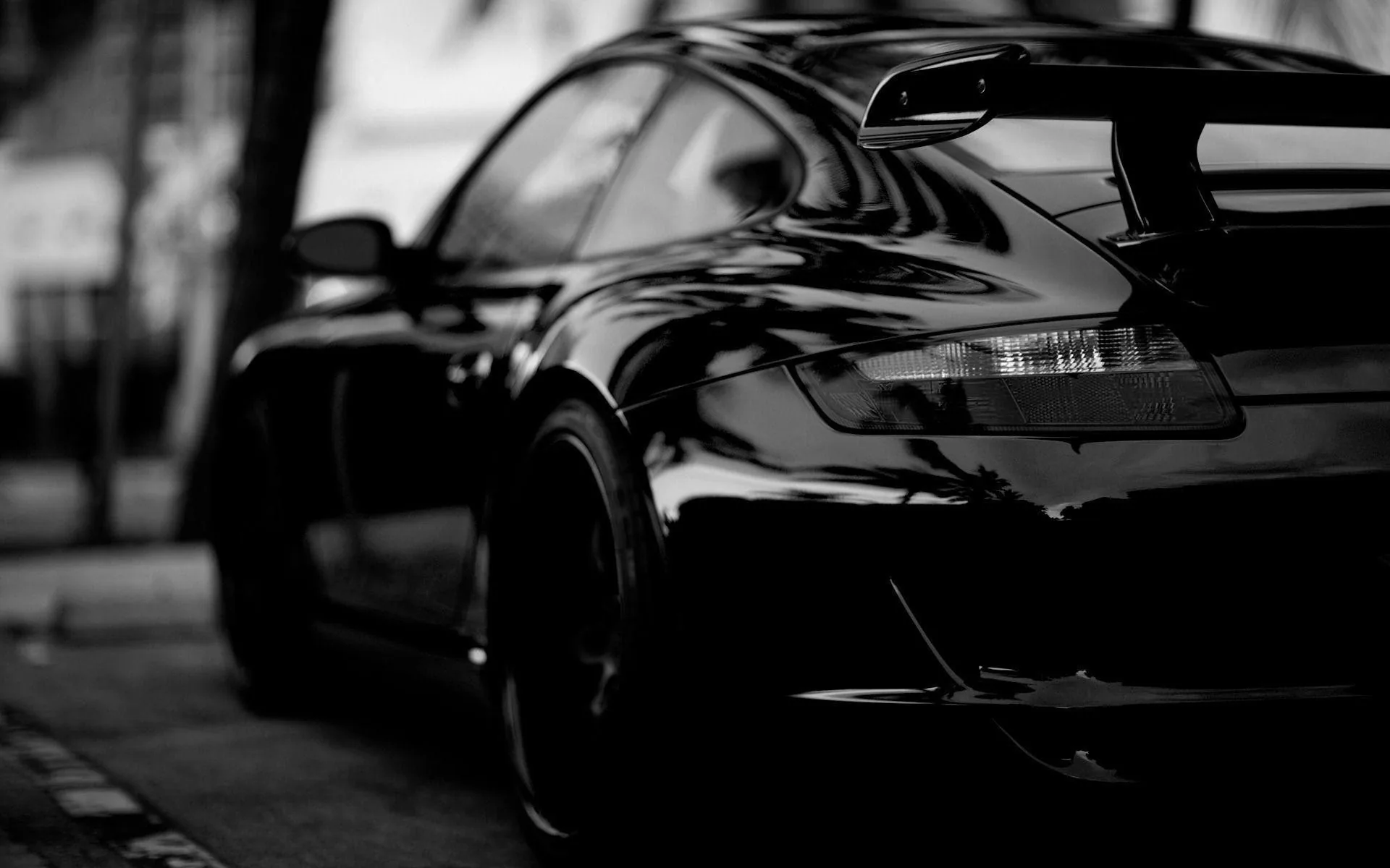 Black and white close-up of a 911's tail, gloss paint bending the reflections of the buildings while the wing and tail lamp fade into shallow focus.