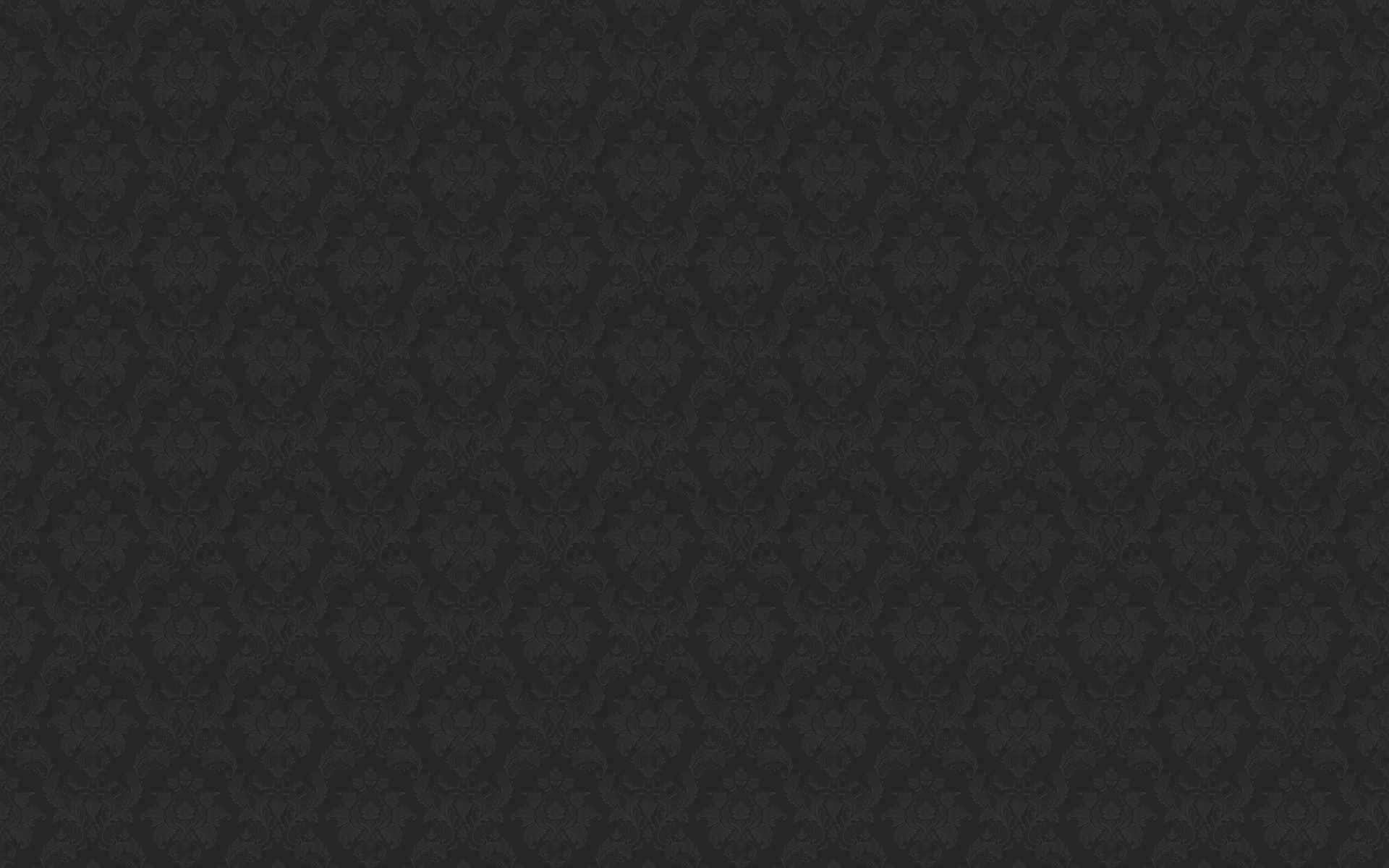 A small repeating motif pressed into flat charcoal, barely raised so the pattern only shows where the light grazes across it.