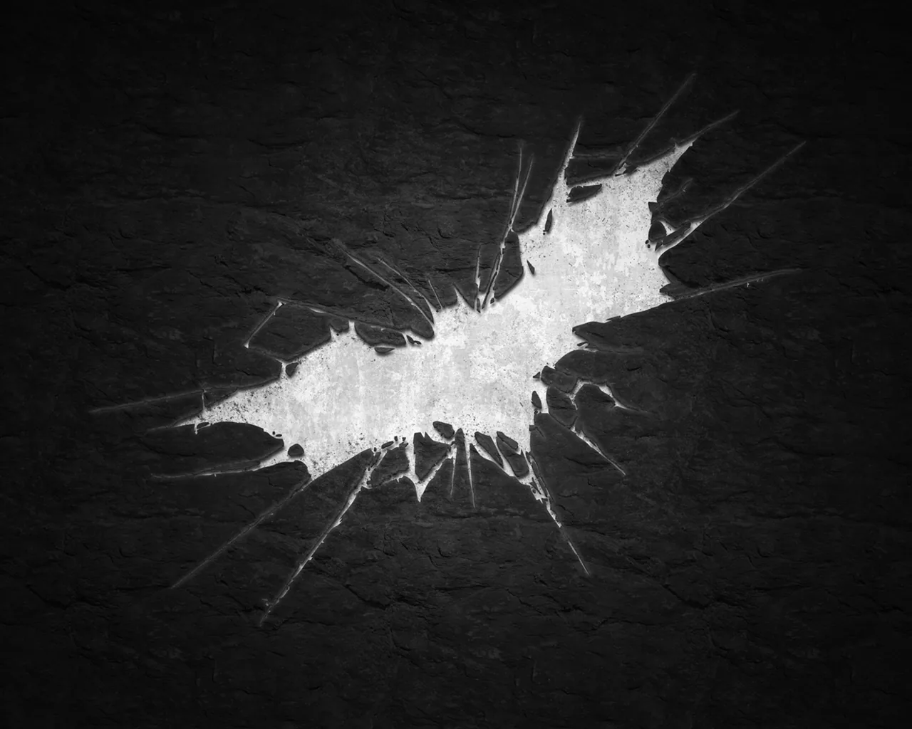 The Dark Knight Rises bat emblem breaks through a dark stone wall like shattered glass, cracks radiating outward while both lower corners stay clean for desktop icons.