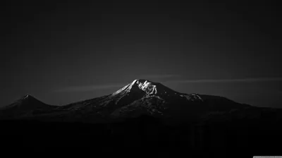 A lone snow-covered peak catches the last light while the valley and sky fall away into deep monochrome black.