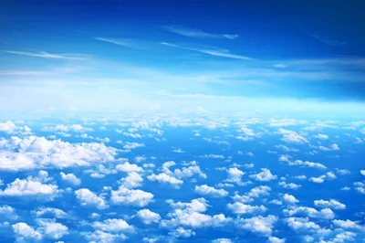 Scattered white clouds seen from above, as if from a plane window, thinning toward a bright blue horizon across the middle of the frame.