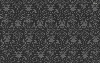 A dark charcoal wall covered in damask motifs only a shade lighter than the ground, the pattern surfacing quietly under a fine woven grain.