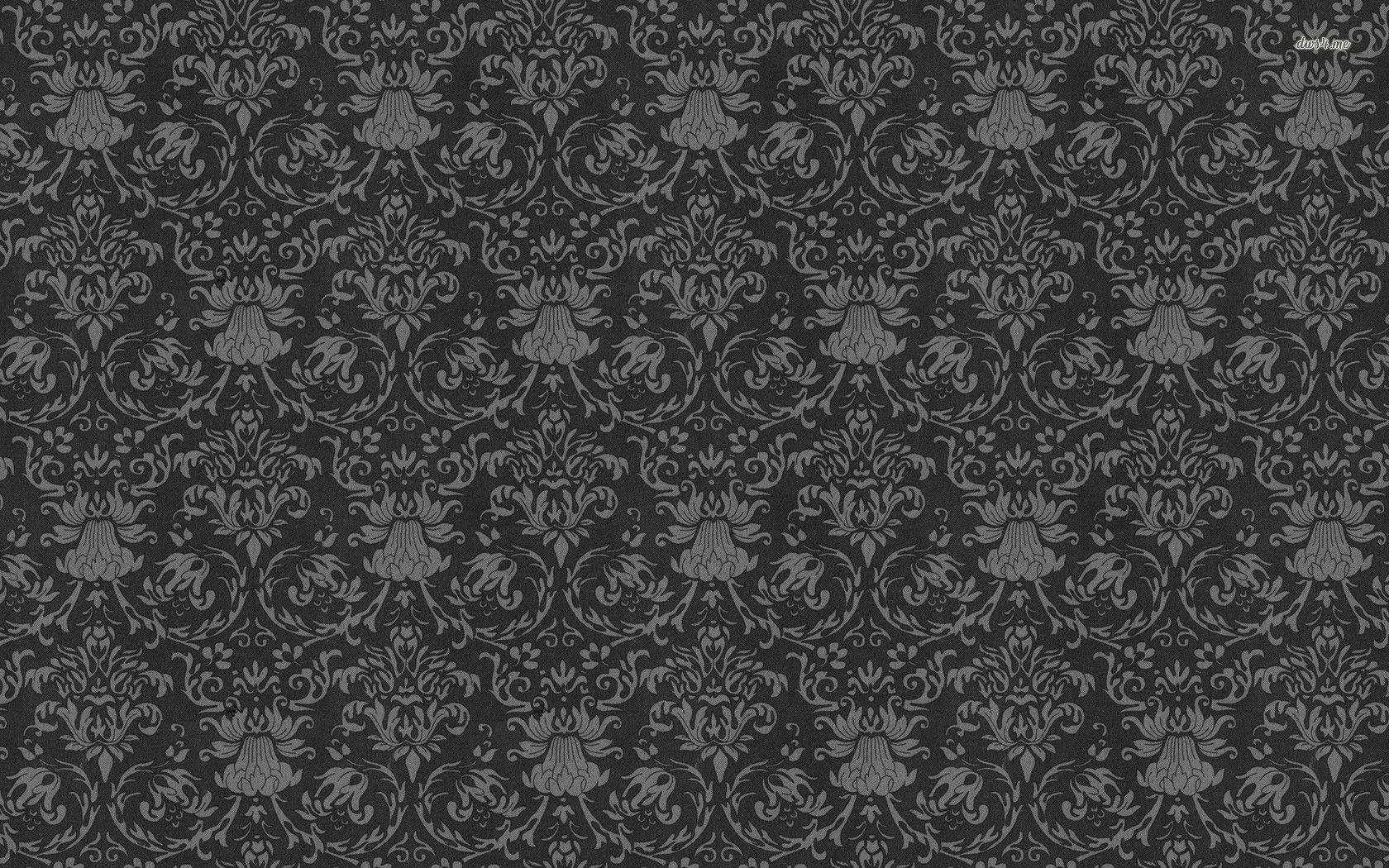 A dark charcoal wall covered in damask motifs only a shade lighter than the ground, the pattern surfacing quietly under a fine woven grain.