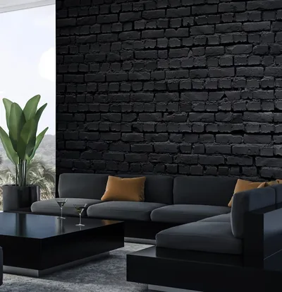 A deep grey sectional runs along a painted black brick wall, daylight entering from a window on the left edge.