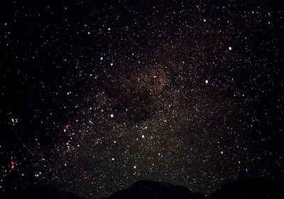 A mountain ridge cuts a black line along the bottom while the Milky Way rises overhead, faint red nebulae glowing near the left edge.