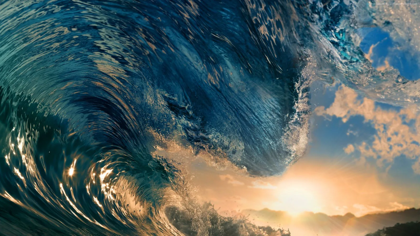 A heavy wave folds over mid-break, its face turned gold by low evening sun breaking through clouds behind it.