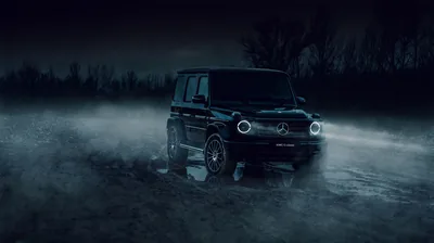 The boxy G-Wagon sits on wet ground with mist rolling past its wheels, only the round headlights and a treeline showing against the blue-black night.