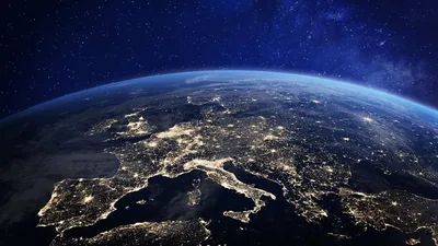 Italy, the Alps and the Mediterranean glow with city lights under thin cloud, the curve of the atmosphere fading into a starry upper edge.