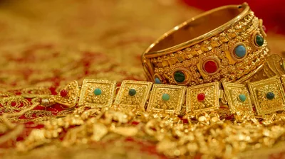 A gold bangle rests on a choker set with red and green stones, all laid over deep red cloth with the background melting into blur.