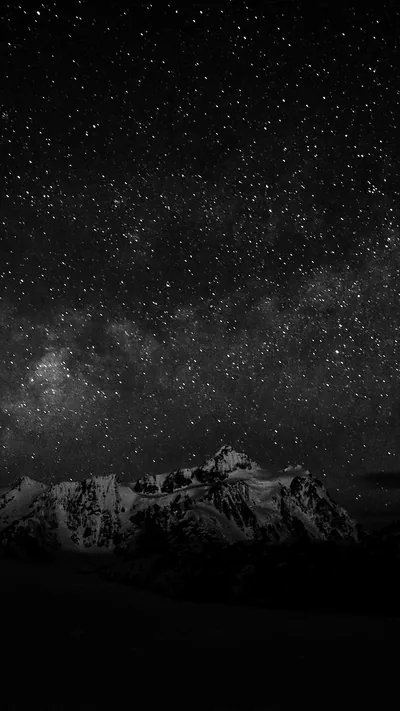 The Milky Way spills across a monochrome night sky, with a jagged snow-dusted ridge sitting low along the bottom and nothing but stars above.
