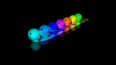 Seven small spheres line up in a diagonal row from blue to red, each one lit from within and mirrored in the glossy black surface below.