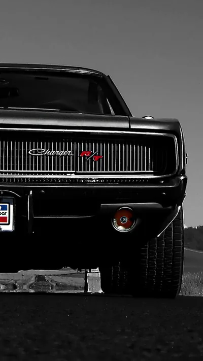 The blacked-out grille and hidden headlamps of a classic muscle car fill the lower half of the frame, chrome badges and a round rear lamp catching what light there is.