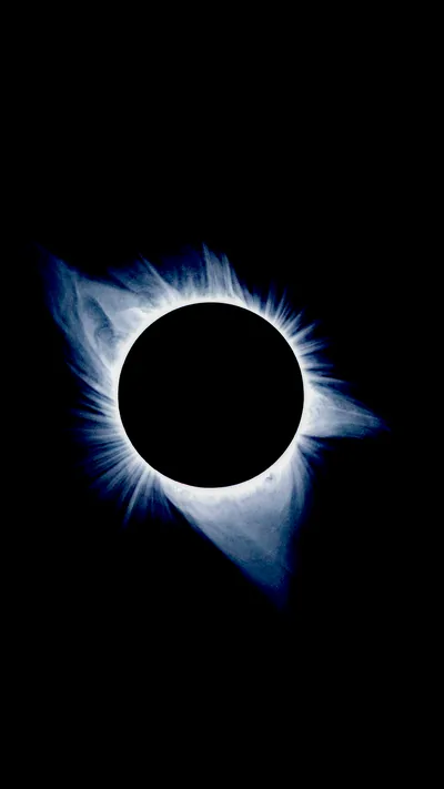 The moon sits as a black disc while a blue-white corona flares unevenly around it, longer streamers reaching down to the left.