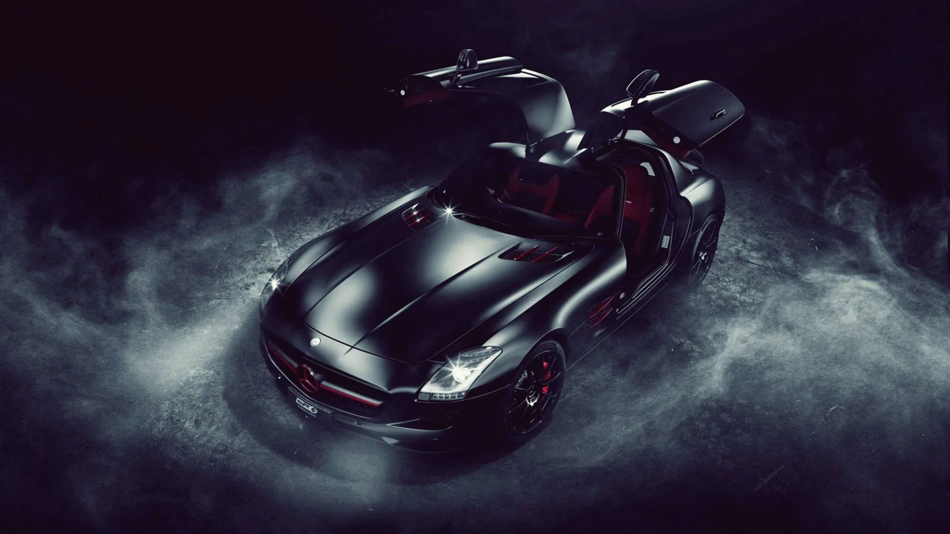 A black Mercedes SLS with both doors raised, thick smoke rolling around the wheels and a red leather interior just visible through the open cabin.