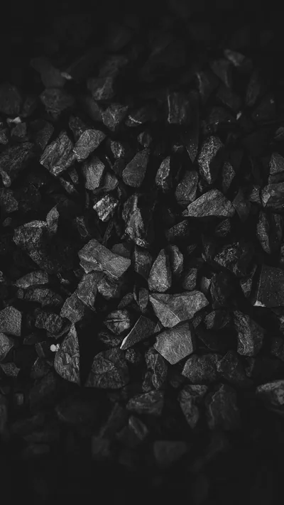 Sharp broken stones packed edge to edge in monochrome, light catching only the upper facets while the bottom fades out.