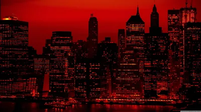 Skyscrapers crowd the waterfront under a solid red sky, their windows the only pinpricks of light across an otherwise black mass.