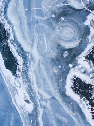 Pale slate stone laced with foamy white veins, a circle of concentric rings sitting upper right and black hollows breaking through along both side edges.