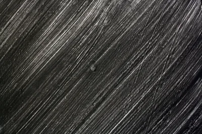 Close-up of dark timber with long diagonal grain, the raised fibres catching white light while the grooves stay black.