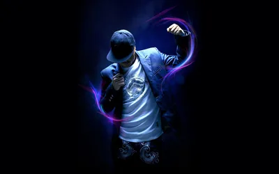 A boy in a denim jacket and cap dances while ribbons of purple and blue light curl around his arms on a near-black stage.