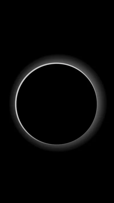 A black disc fills most of the frame with a thin corona glowing all the way around it and fading into empty sky.