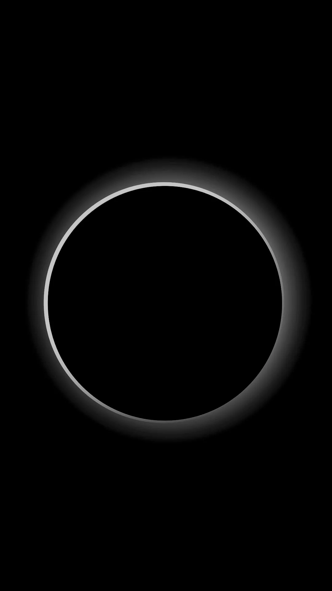 A black disc fills most of the frame with a thin corona glowing all the way around it and fading into empty sky.