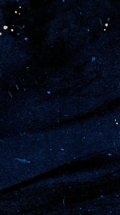 Close-up of dark indigo fabric with pale flecks and a few gold specks in the top corner, the weave creasing softly down the right.