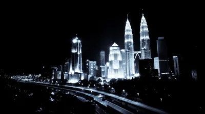 Twin towers and a lit highway glow cold blue against a black sky, traffic trails running out of the bottom corner.