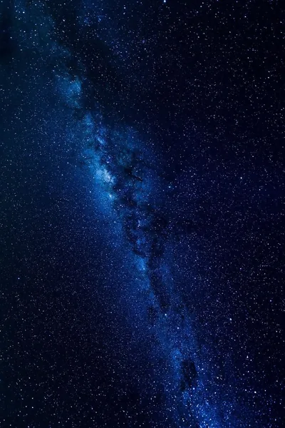 The Milky Way's dust lane rises through the left side of this deep blue vertical star field, thinning out toward the bottom right corner.