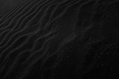Wind ripples run in parallel across dark sand, individual grains catching light along the top of each ridge.